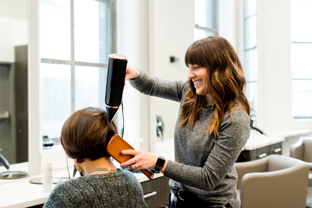 Profissional a secar o cabelo de uma cliente num salão iluminado